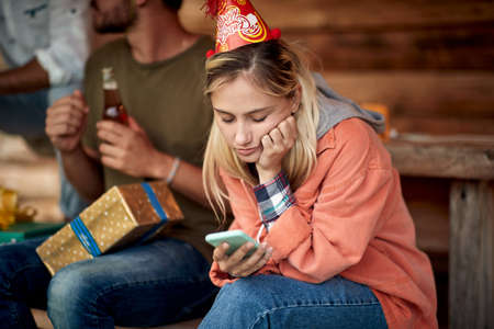 Girl feeling bored on birthday party. Sitting and looking at phone. Birthday, celebration, holiday.の写真素材
