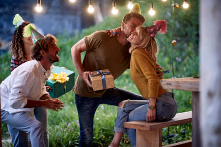 A young girl is getting presents and congratulations from friends at her birthday party at cottage porch on a beautiful day. Vacation, nature, cottage, celebrationの写真素材
