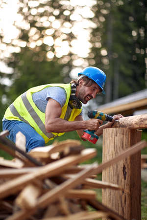 A young male builder working at a construction site in the forest on a beautiful day. Construction,...