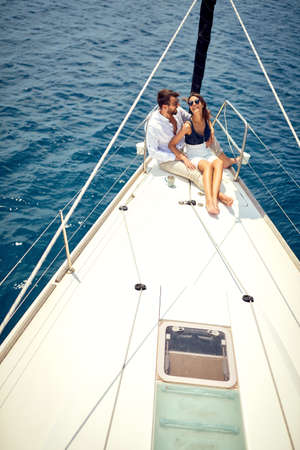 A young couple in love is sitting in a hug on the bow of the yacht and having a good time while ride...