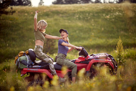 Two young sexy girls enjoy riding the quad on a beautiful sunny day in the nature. Riding, friendship, nature, activityの写真素材