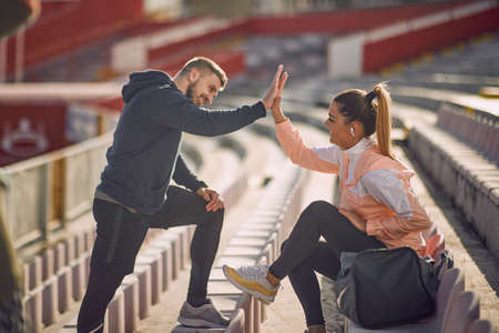 beardy guy and beautiful female giving high-five to each other at the stadium in sportswear,  smilingの写真素材