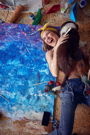 Young sexy female artist playing with her dog in the studio