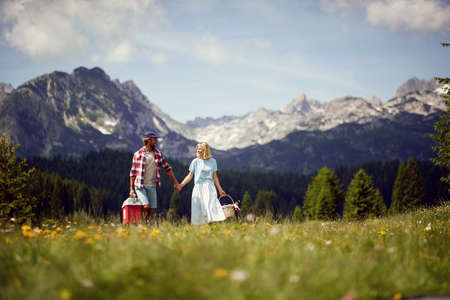 Couple walking together with picnic baskets on green meadow. Fun, togetherness, lifestyle, nature concept.の写真素材