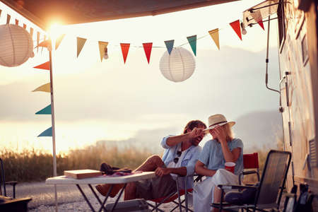 Couple in love. Sitting in front of camper rv. Having fun. Outdoors summer party. Fun, togetherness, nature concept.の写真素材