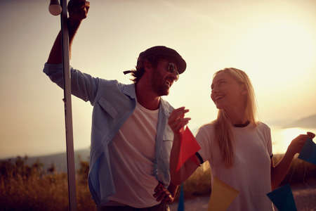 Couple putting up decoration on camper rv. Decoration for party. Fun, togetherness, nature concept.の写真素材