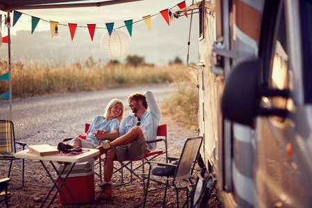 Couple in love, sitting and smilling at each other in front of camper rv. Fun, travel, togetherness, love concept.の写真素材