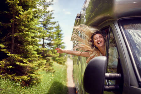 Blonde woman on the window of an rv with hands out smiling enjoying ride.Transport, roadtrip, nature concept.の写真素材