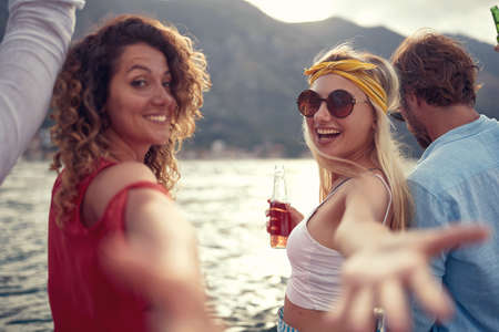 Young friends sitting on pier talking, laughing and drinking beers.