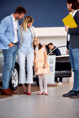 Family in car sales salon standing with salesman near new carの写真素材