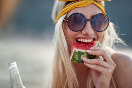 Smiling girl with sunglasses enjoys the lake and eats a watermelonの写真素材