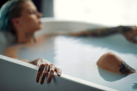 A young beautiful tattooed girl enjoying a warm bath in a relaxed atmosphere in the bathroom. Relaxation, bath, bathroom, homeの写真素材