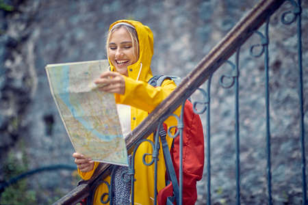 Traveler smiling girl   with map in vacation.
Happy female in yellow raincoat and map enjoying rainy dayの写真素材