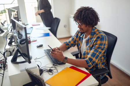 A young man is using a smartphone at the job in a pleasant atmosphere in the office. Employees, job, officeの写真素材