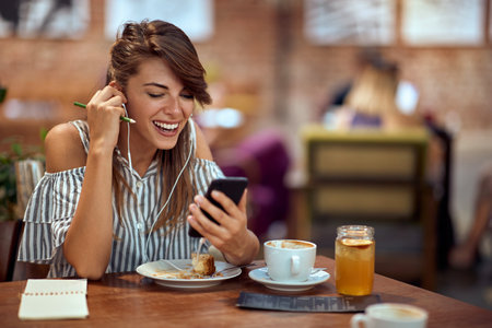 Cheerful young woman on a video call with friend while she is in cafe alone, enjoying coffee break. Fun, lifestyle, lesiure concept.の写真素材
