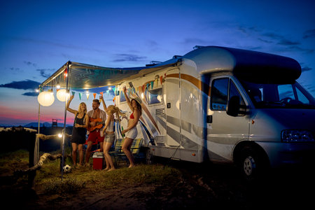 Fun with friends in camp, in front of rv. Young group of people dancing, playing guitar, and...