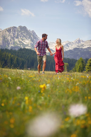 Beautiful young couple holding hands and running on green meadow. Fun, togetherness, lifestyle, nature concept.の写真素材