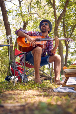 Smiling man camping  on the nature and playing guitarの写真素材