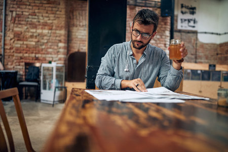 Handsome young man with glasses holding drink and reading newspaper in modern cafe. Young man relaxing alone.の写真素材
