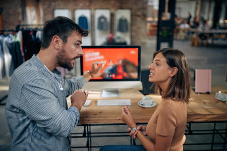 Man and woman having serious conversation at work, in front of desktop computer and work desk in a clothing shop. Business meeting, brainstorming, teamwork, boss and emloyee meeting.の写真素材