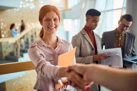 Close-up of a young business woman who is handshaking while standing in a pleasant atmosphere in the hallway with colleagues. Business, people, companyの写真素材