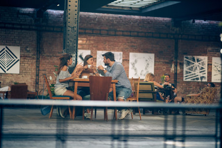 Group of friends having coffee and talking in a modern cafe. Two young women and a man enjoying...