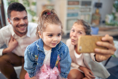 Family's special moment of taking a selfie together.  Mother, father, and their daughter, are close together with big smiles on their faces. The mother holds up her smartphone, capturing the happy moment, while the father and daughter lean in and pose for the picture. The love and togetherness between the family members is palpable, and the photo is a beautiful representation of the joy and warmth that comes from spending quality time with loved ones.の写真素材