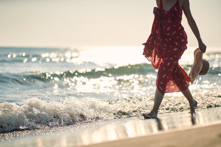 A young woman enjoys barefoot walk through the shallow on the beach on a beautiful summer day. Summer, beach, sea, vacationの写真素材