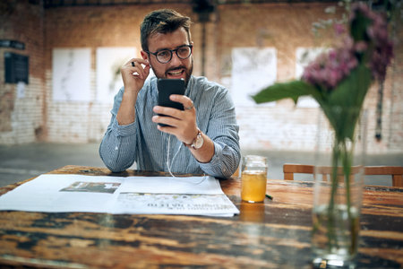 Young attractive man sitting in cafe, with headphones using smartphone. Modern cafe background.の写真素材