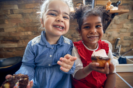 The heartwarming connection of friendship as two young girls share laughter and indulgent muffins in the kitchen.の写真素材