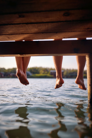 Shot of a barefoot young couple sitting on the dock on the river on a beautiful summer day. Summer, river, vacationの写真素材