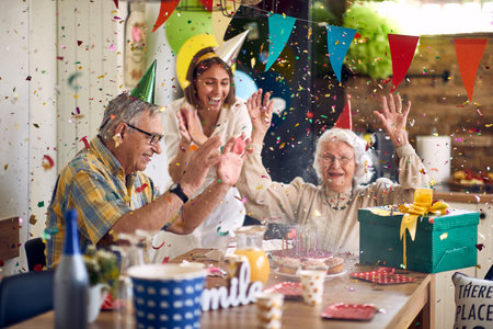 Happy family of senior couple and daughter cheering for birthday senior woman, celebrating her birthday together, together in the home kitchen by dinner table. Home, lifestyle, lifestyle concept.の写真素材