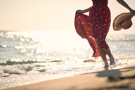 Woman in red dress walking on the sand beachの写真素材