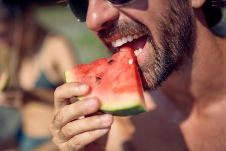 Close up shot of man eating watermelon fruit on beach. Couple on holiday. Holiday, togetherness, lifestyle concept.の写真素材