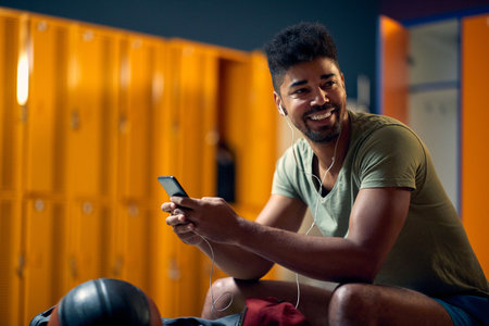 Smiling young man using smatphone in gym dressing room before workout. Sport, active, lifestyle concept.の写真素材
