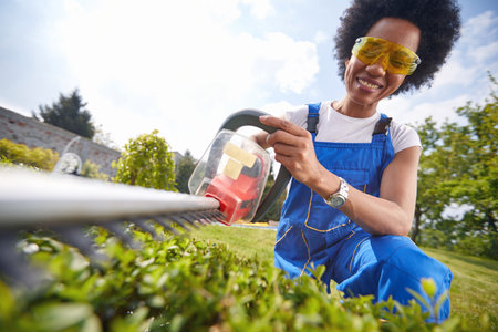 Woman confidently wields a precision trimmer as she skillfully shapes a vibrant living hedge. With a...