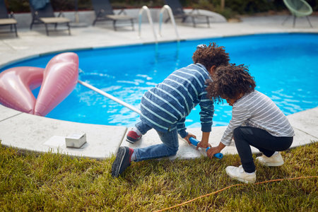 Two little african american kids playing by the pool, cleaning with net, bonding together. Sister and brother together outdoors. Familyu, lifestyle, togetherness concept.の写真素材