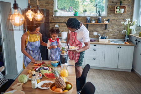 Afro-American family comes together to prepare a meal in their kitchen. The image showcases a mother, father, and daughter working collaboratively, surrounded by culinary ingredients and utensils.の写真素材