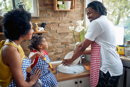 Cute little girl blowing bubbles in the kitchen by the sink, while her father is washing dishes. Cheerful family together. Home, family, lifestyle concept.の写真素材