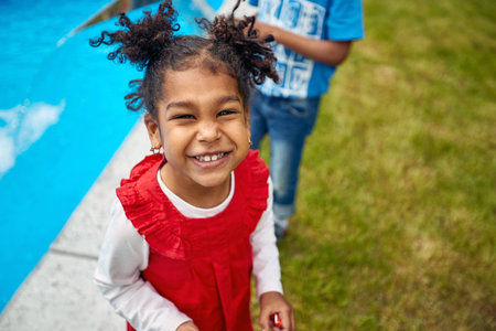 Afro-American girl, dressed in a vibrant red dress, enjoying a moment of pure joy by the poolside. Her infectious laughter fills the air as she revels in the sunny ambiance.の写真素材