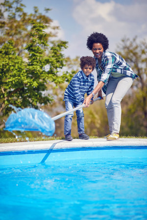 Young mother and son cleaning the pool with a cleaning net together standing by the pool, working as a team. Togetherness, lifestyle, family concept.の写真素材