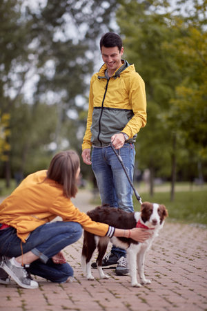 young caucasian male standing with his dog on a leash looking at female, smiling
