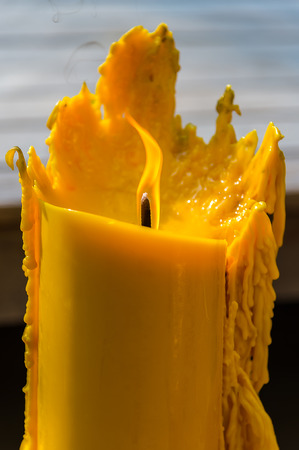 Yellow candle with flame and melting waxの写真素材