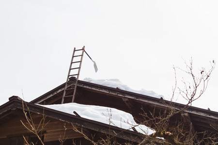 shovel hanging on ladder with snow on the roofの写真素材