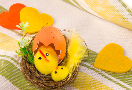 Easter decoration: hen with chicken in the nest and three felt hearts on cotton napkin. Main colors:...