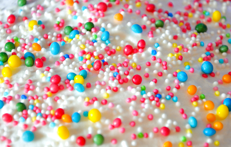 Top of Easter cake covered with white icing and sprinkled with color pops. Candy background.
