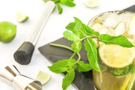 Black serving slate platter with sweaty glass of mojito cocktail, drink making tools, lime and mint...