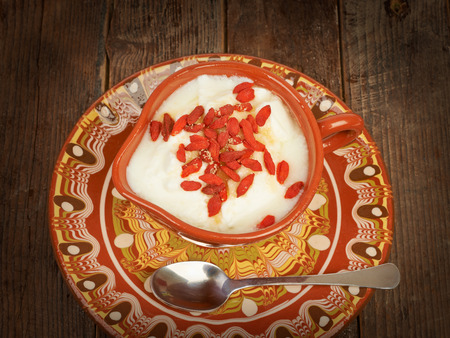 Yogurt with goji berries in a ceramic pot on a wooden tableの写真素材