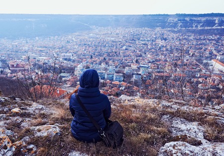 Young woman in a coat sitting on the ground. City view with mountains in Provadia in Bulgariaの写真素材