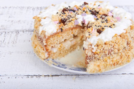 Biscuit cake with crumbs, whipped cream and concentrated milk on white wooden background